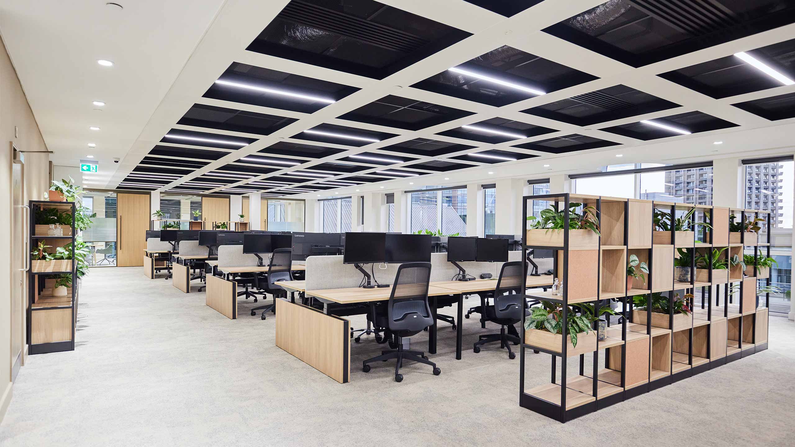 Open-plan office with rows of workstations, ergonomic chairs, and biophilic shelving dividers at 24 Chiswell Street by ODCreate.
